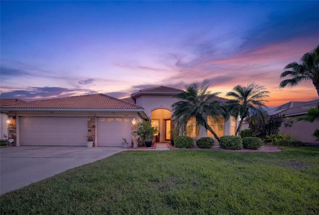 A single-story suburban house with a two-car garage, tile roof, and palm trees at sunset — 4612 E 62 AVENUE, BRADENTON, FL