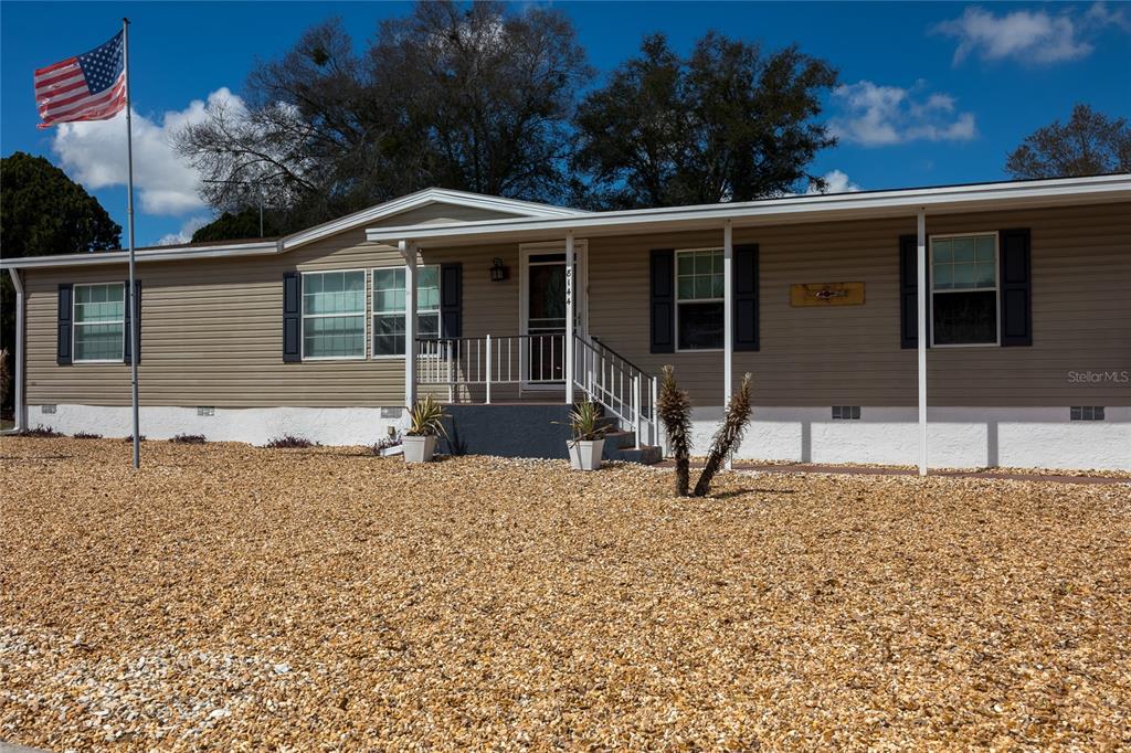 A single-story manufactured home with tan siding, dark shutters, and a gravel front yard — 8144 WEATHERFORD AVENUE, BROOKSVILLE, FL