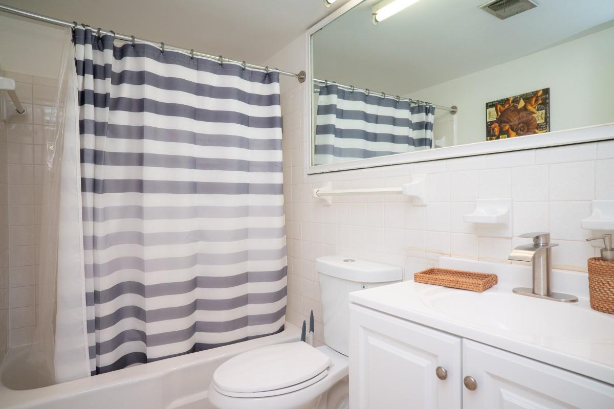 A bathroom features a white vanity, a toilet, and a shower with a striped curtain — 701 Pine Drive # 107, Pompano Beach FL 33060, POMPANO BEACH, FL