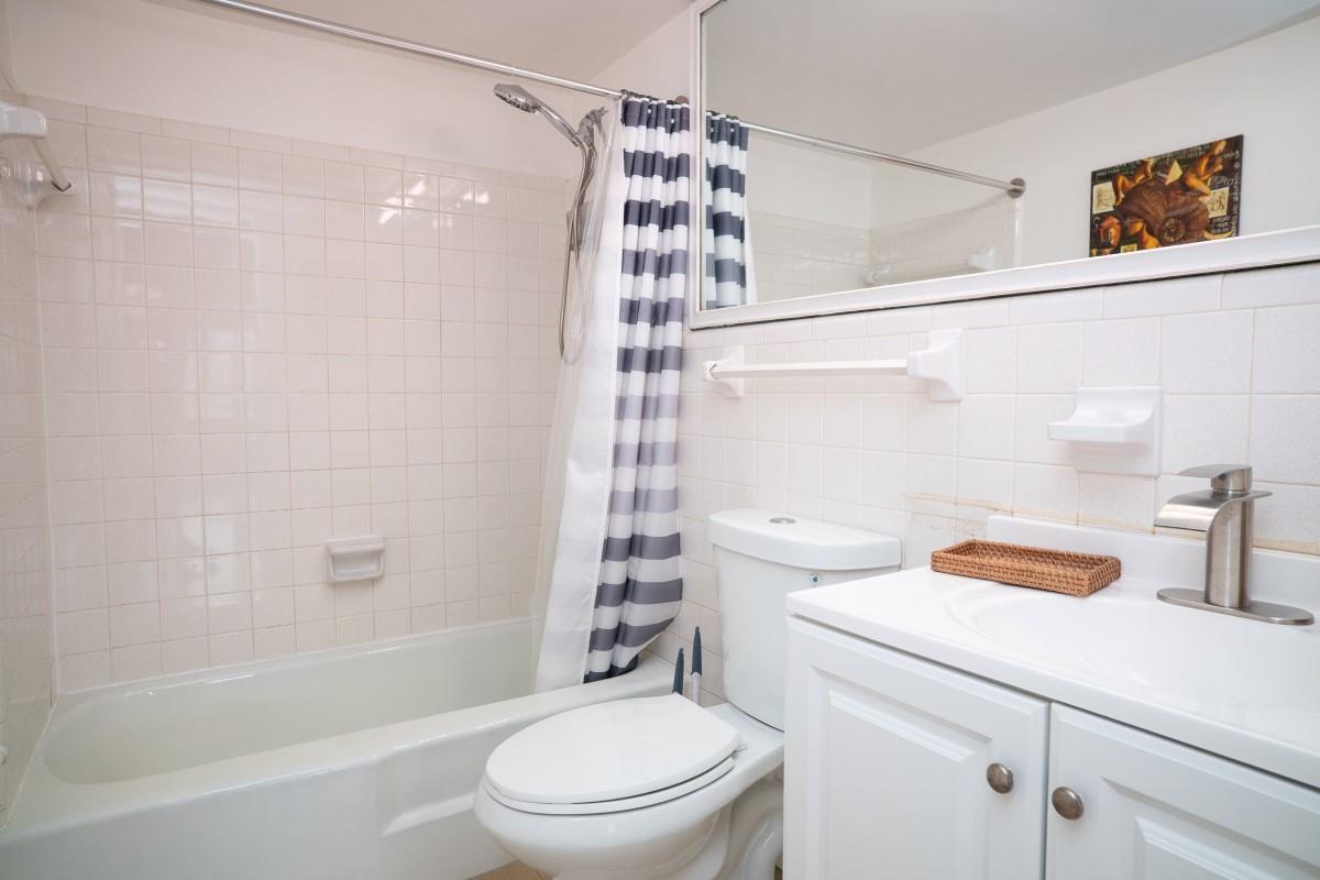 A bathroom featuring a white vanity, a toilet, and a shower-tub combination with tiled walls — 701 Pine Drive # 107, Pompano Beach FL 33060, POMPANO BEACH, FL