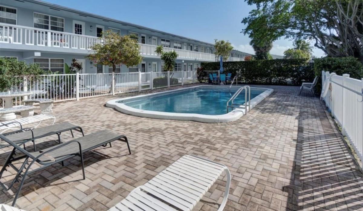 A swimming pool sits on a brick patio in front of a two-story apartment building — 701 Pine Drive # 107, Pompano Beach FL 33060, POMPANO BEACH, FL