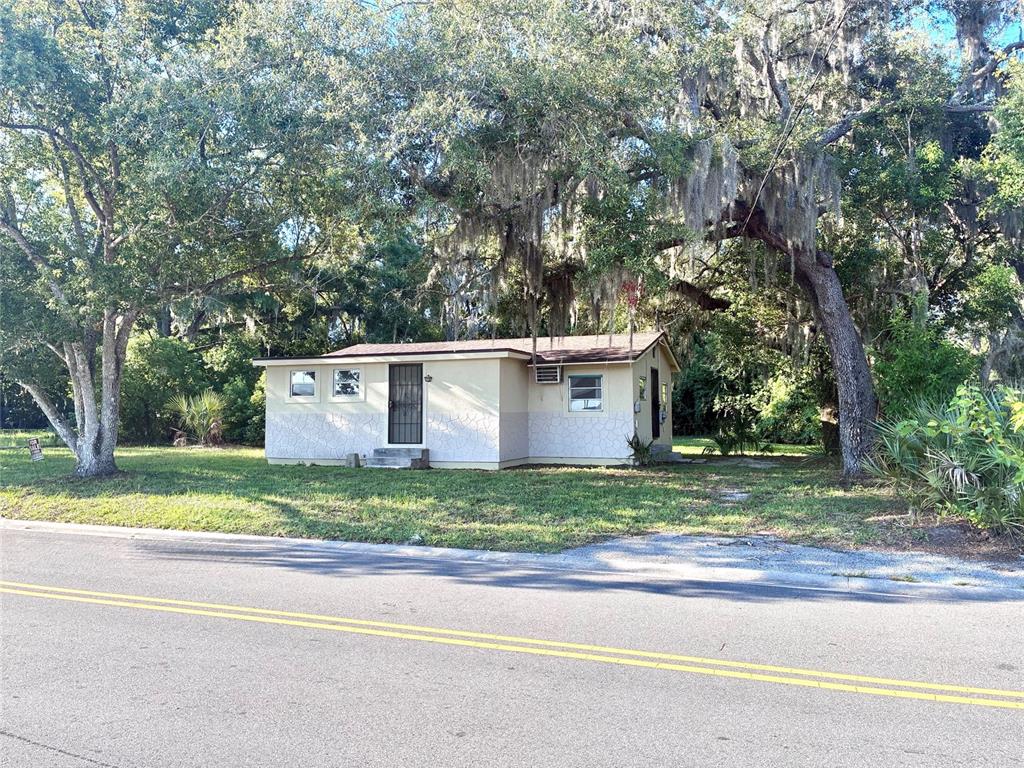 A beige, single-story house with a metal door and several windows sits on a grassy lot — 2024 DIXIE AVENUE, EUSTIS, FL