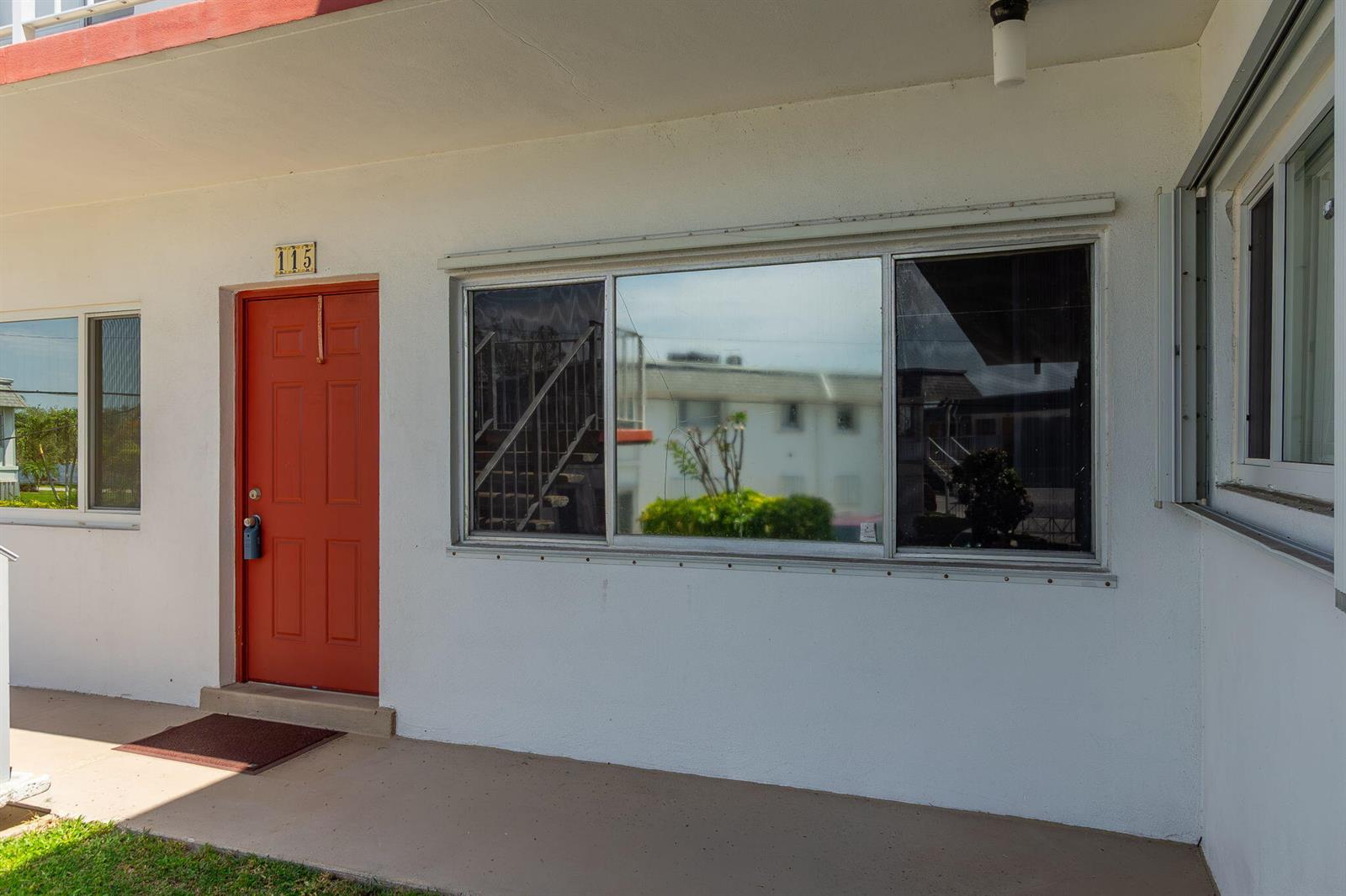 The exterior of a white building features a red front door numbered 115 — 3120 Cynthia Lane # 115, FL 33461, FL