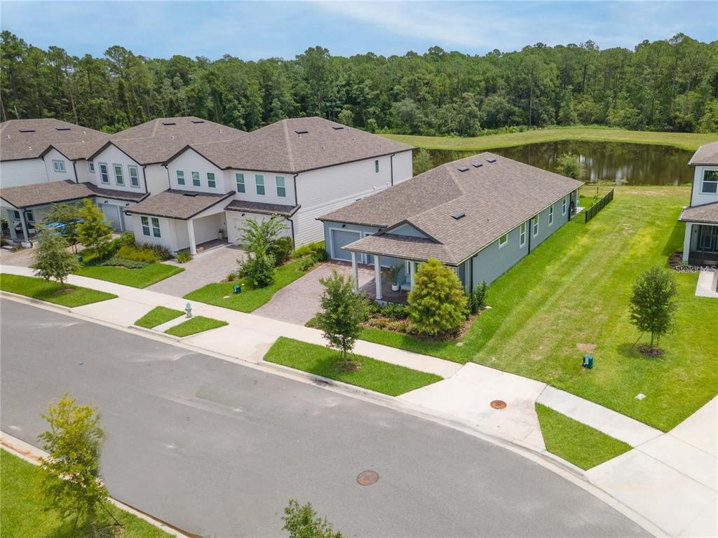 An aerial view shows suburban townhouses with gray roofs and green lawns near a pond — 11243 PIXIE MANDARIN COURT, WINTER GARDEN, FL