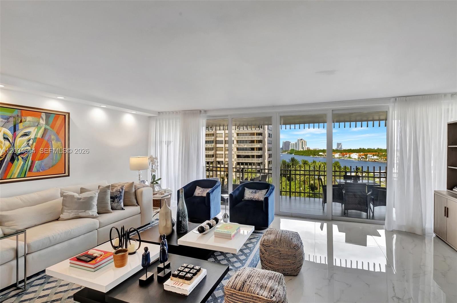 A modern living room features a white sofa, blue armchairs, and a balcony overlooking water — 2 Grove Isle Dr # B706, Miami FL 33133, MIAMI, FL