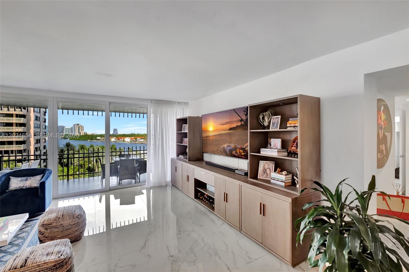 A living room features marble floors, a large media console, and a balcony overlooking water — 2 Grove Isle Dr # B706, Miami FL 33133, MIAMI, FL