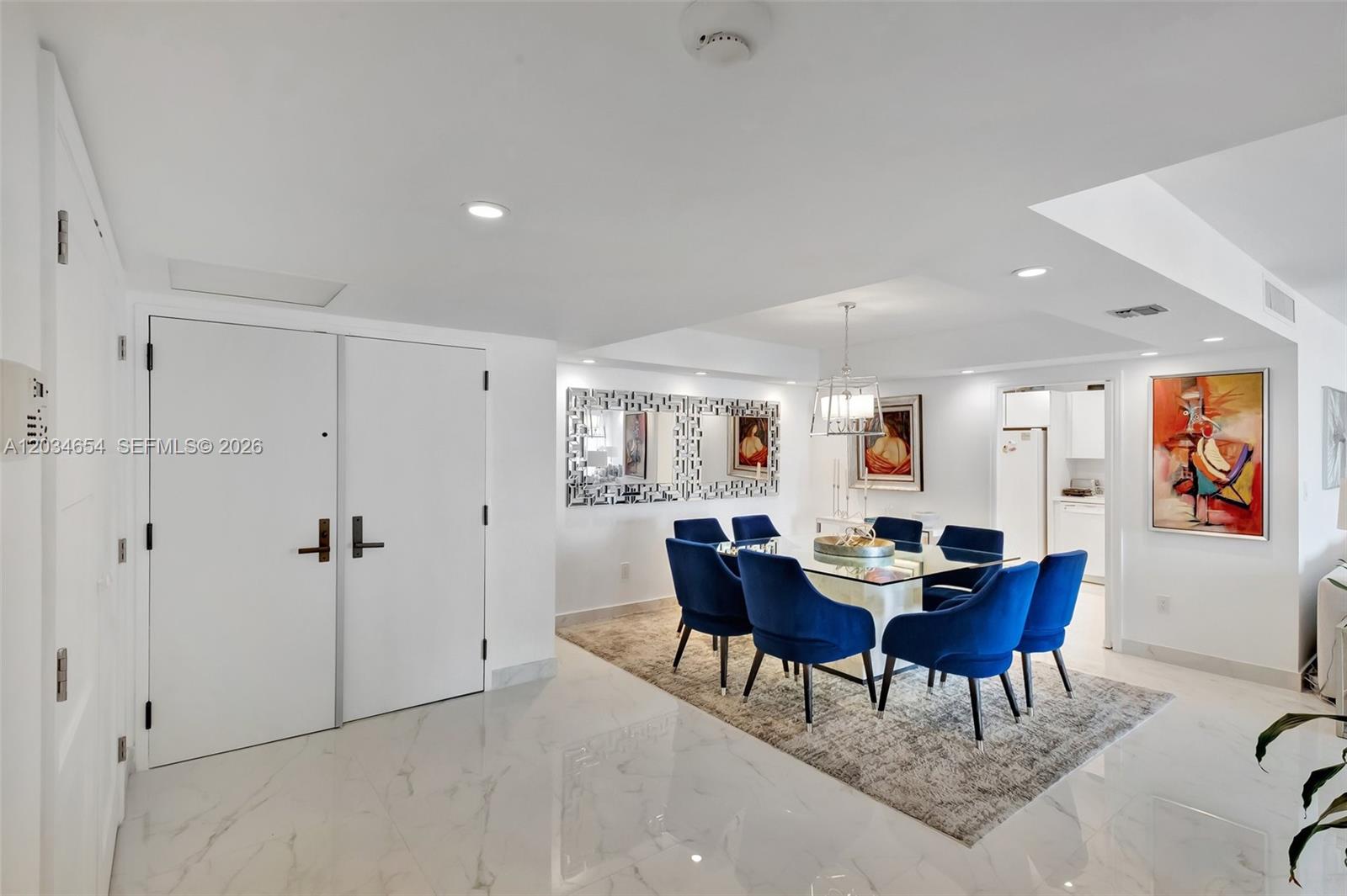 A dining room features a glass table, blue velvet chairs, and a large wall mirror — 2 Grove Isle Dr # B706, Miami FL 33133, MIAMI, FL