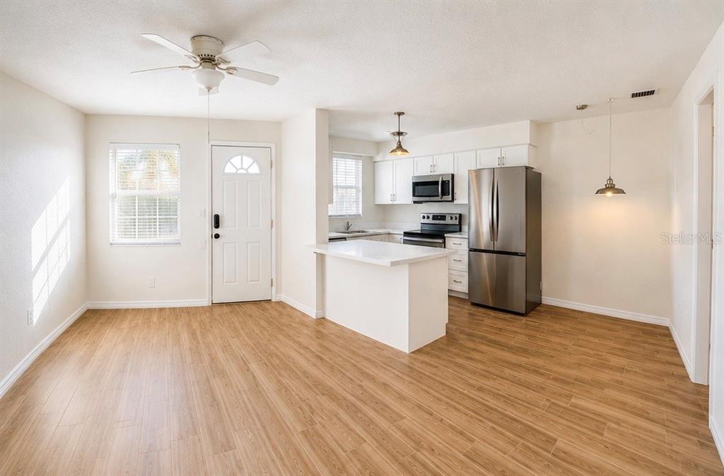 An open-concept kitchen and living area featuring light wood-look flooring and white cabinetry — 9030 BLIND PASS ROAD UNIT D6, ST PETERSBURG, FL