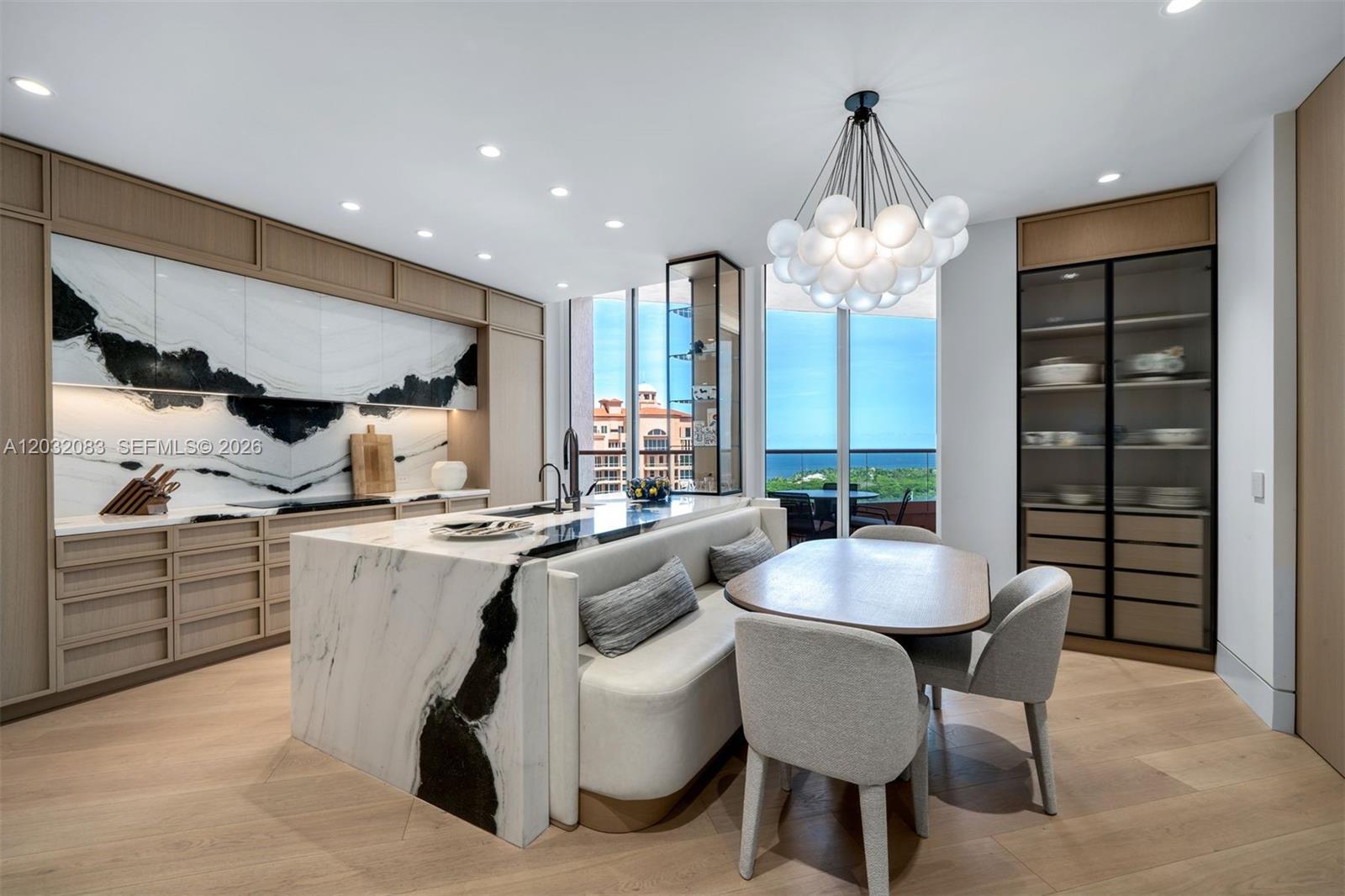 A modern kitchen features a marble island with integrated bench seating and light wood cabinetry — 60 Edgewater Dr # D, Coral Gables FL 33133, CORAL GABLES, FL
