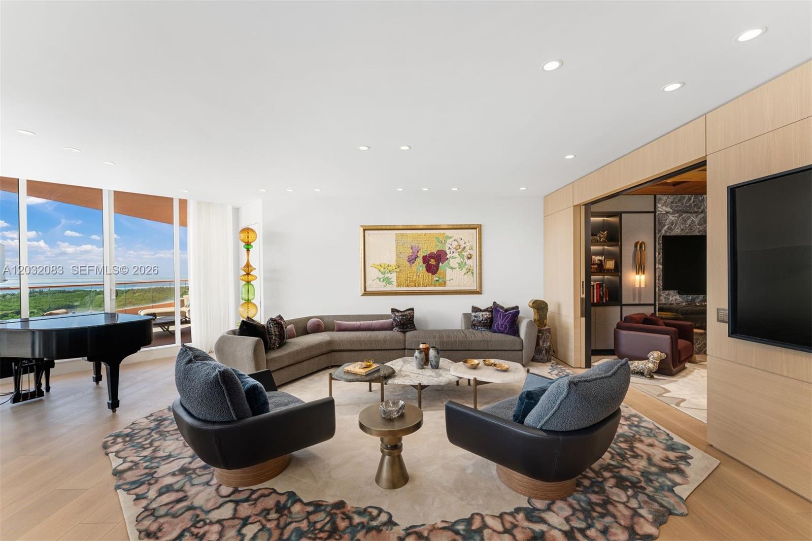 A modern living room features a curved sofa, two armchairs, a piano, and floor-to-ceiling windows — 60 Edgewater Dr # D, Coral Gables FL 33133, CORAL GABLES, FL
