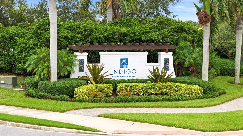 A white monument sign for Indigo at Lakewood Ranch sits in a landscaped garden area — 3036 SKY BLUE COVE, LAKEWOOD RANCH, FL