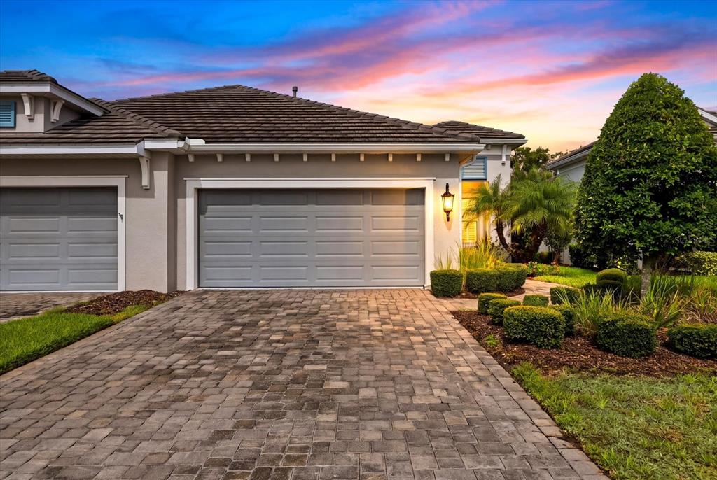 A paved driveway leads to the gray garage doors of a single-story suburban home — 3036 SKY BLUE COVE, LAKEWOOD RANCH, FL