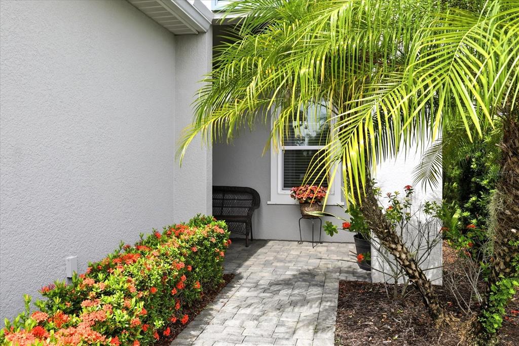 A paved walkway leads to a covered entryway with a bench, window, and palm tree — 3036 SKY BLUE COVE, LAKEWOOD RANCH, FL