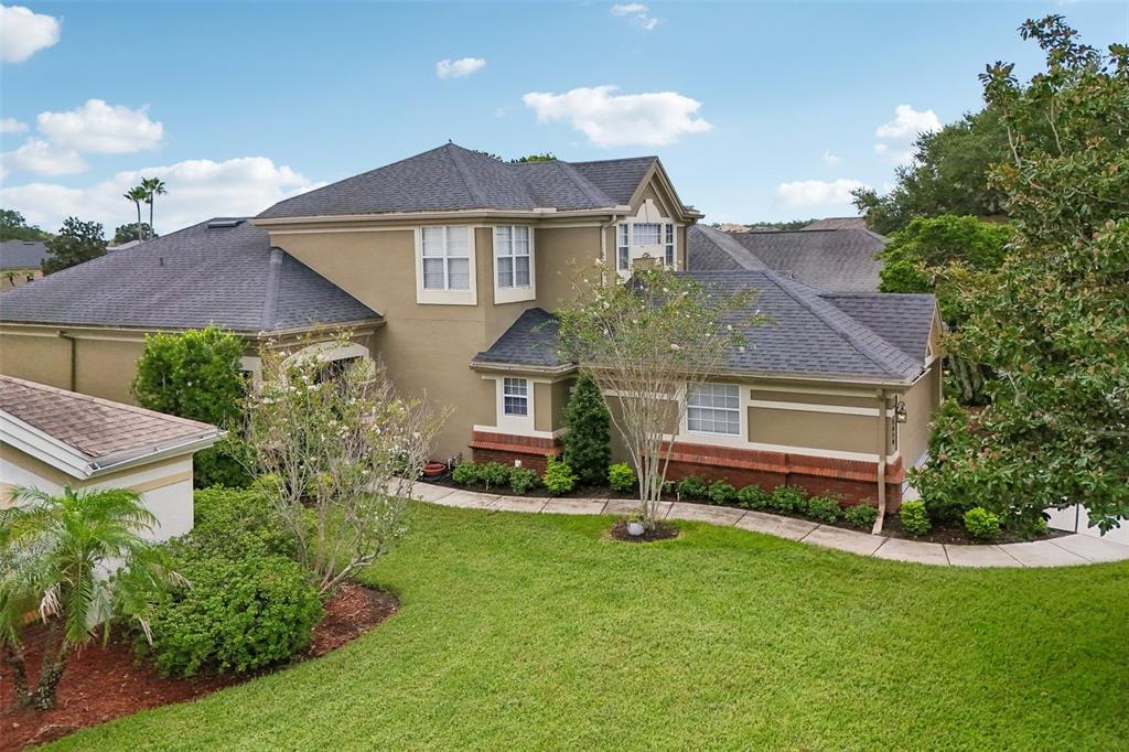 An exterior view of a two-story tan house with a dark shingled roof and landscaping — 3050 SHOAL CREEK VILLAGE DRIVE, LAKELAND, FL