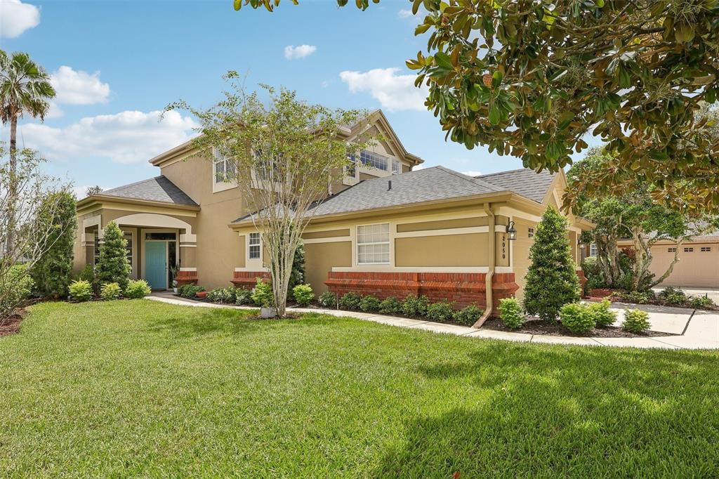 A two-story house with tan stucco walls, brick accents, and a blue front door — 3050 SHOAL CREEK VILLAGE DRIVE, LAKELAND, FL