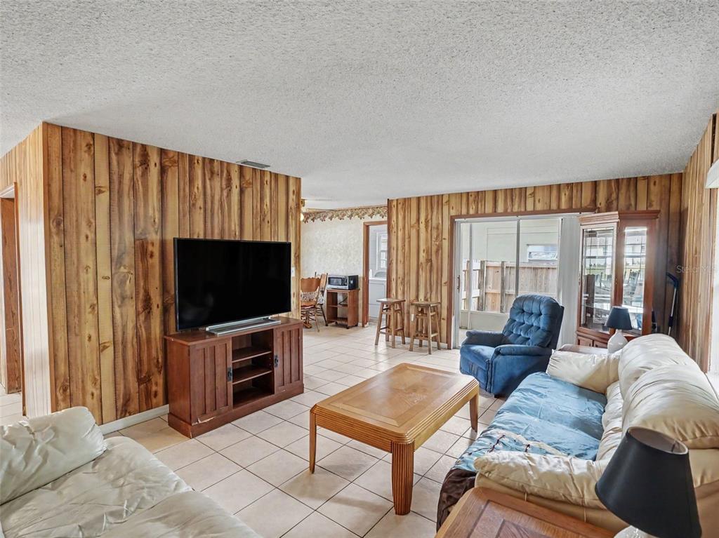 A living room features wood-paneled walls, tile flooring, a television, and a blue recliner — 1609 MAUREEN AVENUE, OCOEE, FL