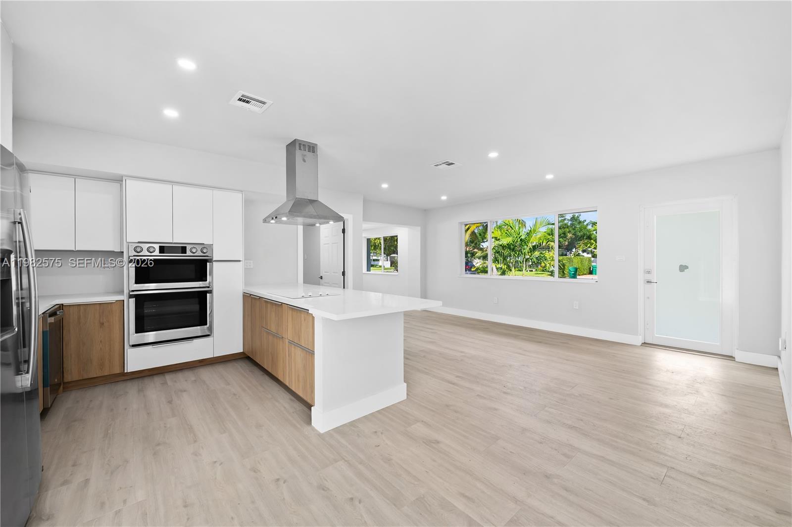 A modern kitchen features white cabinets, wood-toned lower drawers, a central island, and stainless appliances — 8560 SW 126th Ter, Miami FL 33156, MIAMI, FL