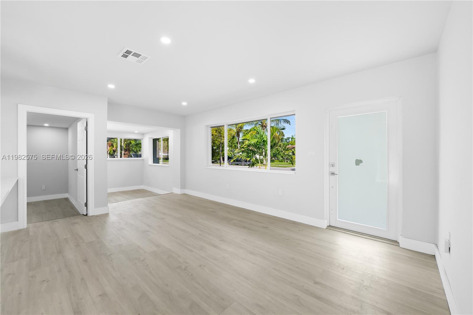 A bright, empty room features light wood-look flooring, white walls, and a glass-paneled exterior door — 8560 SW 126th Ter, Miami FL 33156, MIAMI, FL