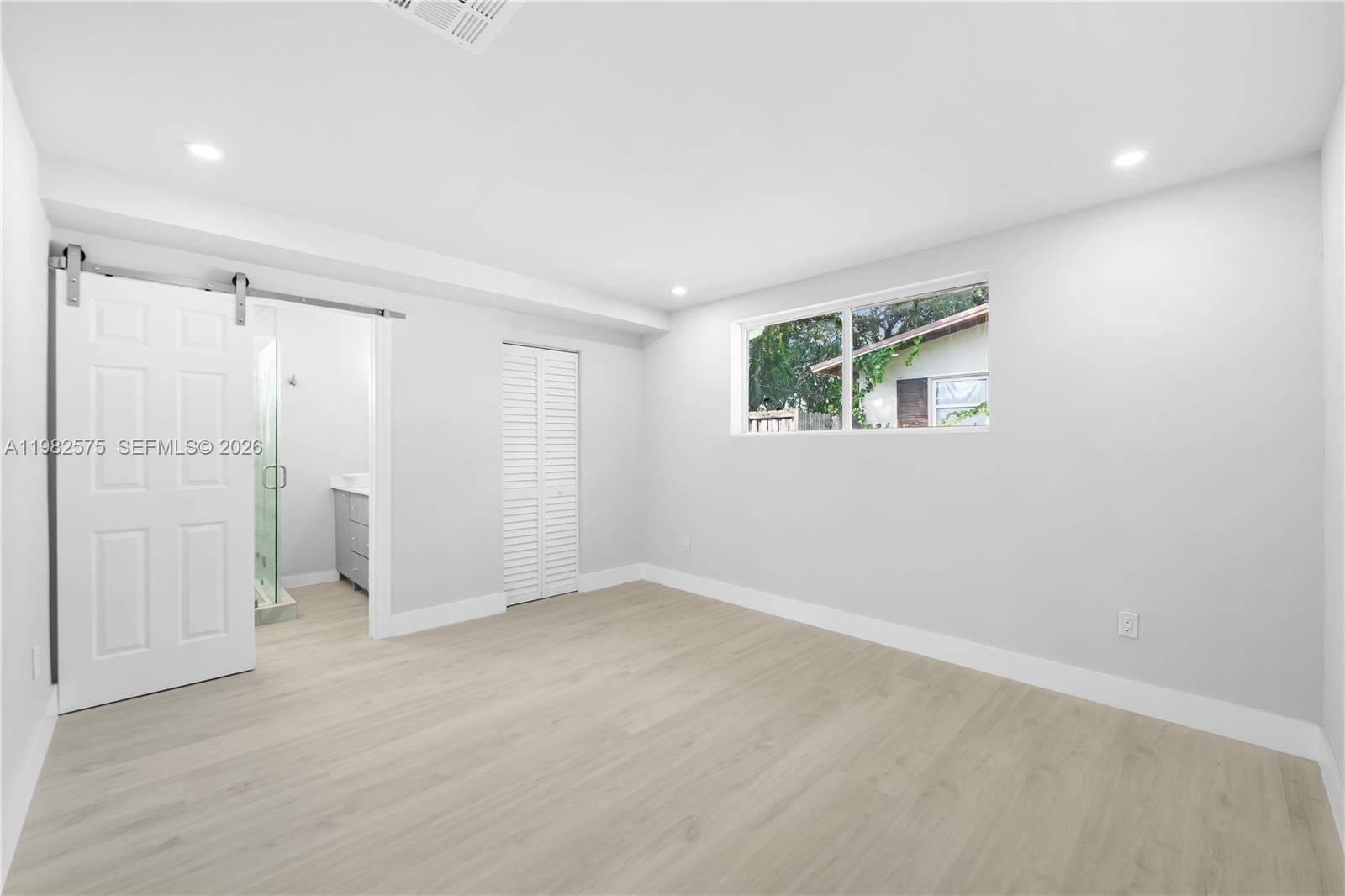 A bedroom features light wood-look flooring, white walls, a sliding barn door, and a closet — 8560 SW 126th Ter, Miami FL 33156, MIAMI, FL