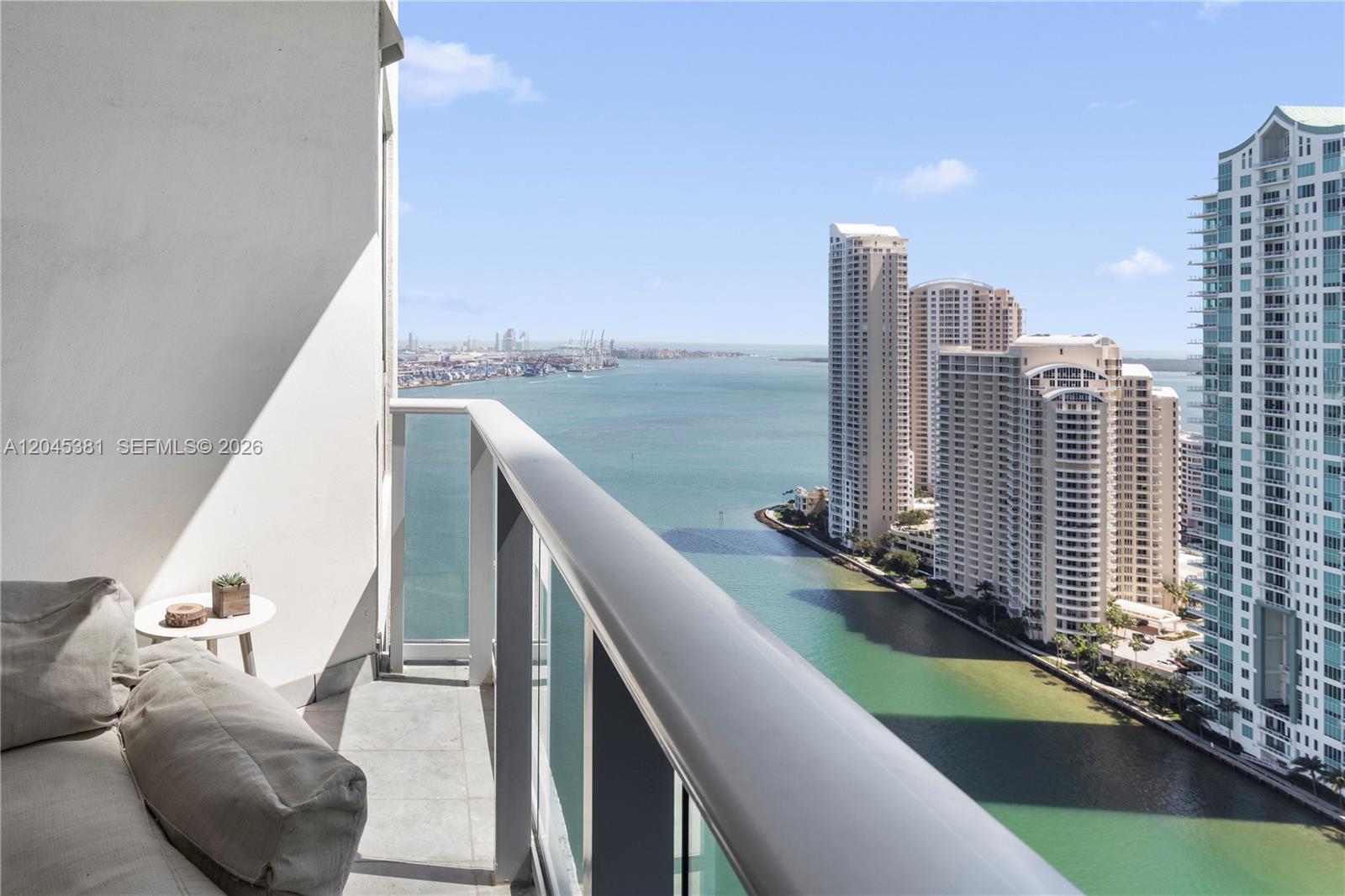 A balcony with a sofa overlooks a bay and high-rise buildings — 300 S Biscayne Blvd # 2806, Miami FL 33131, MIAMI, FL