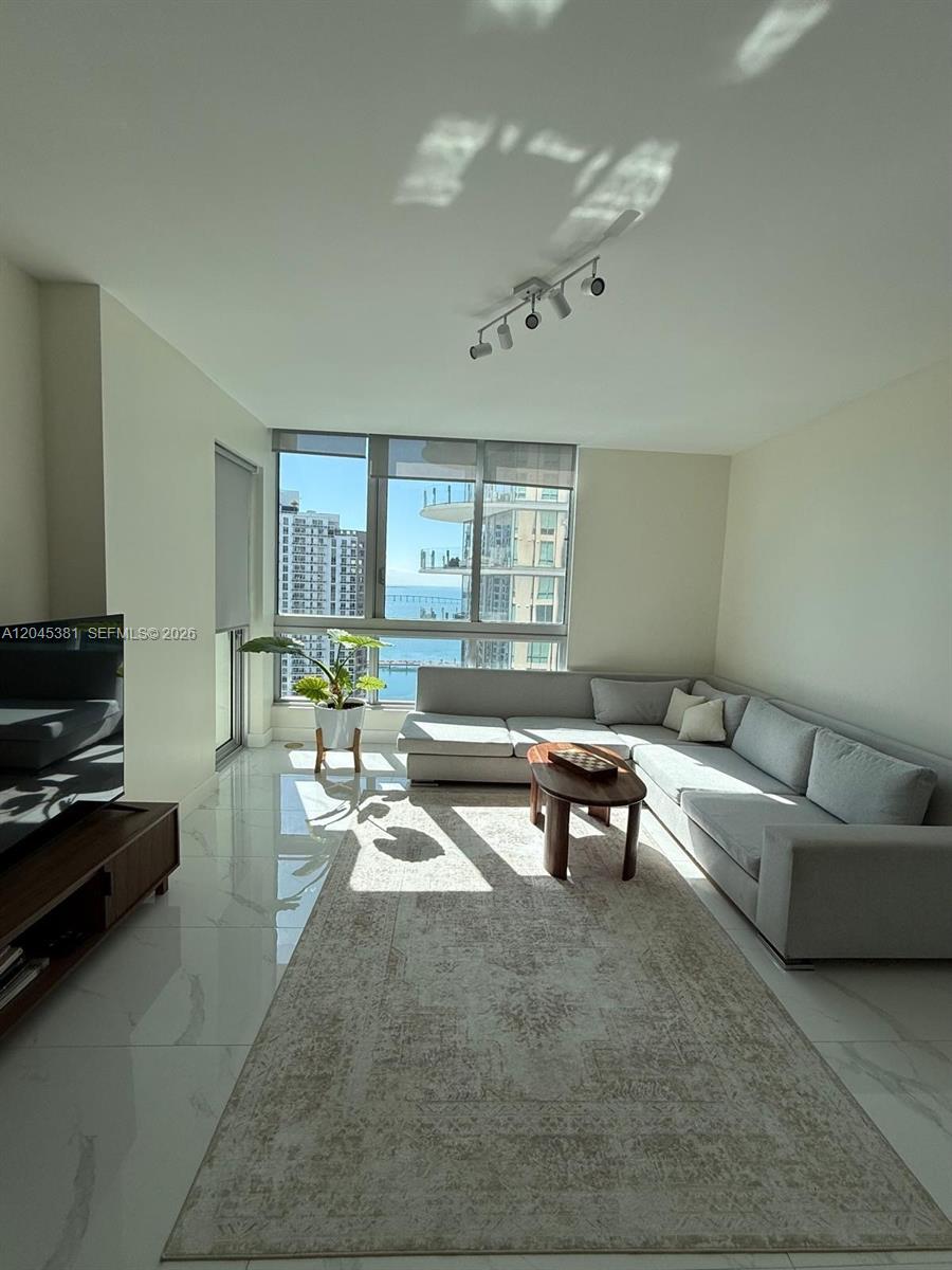 A living room features a light gray sectional sofa, a patterned rug, and floor-to-ceiling windows — 300 S Biscayne Blvd # 2806, Miami FL 33131, MIAMI, FL