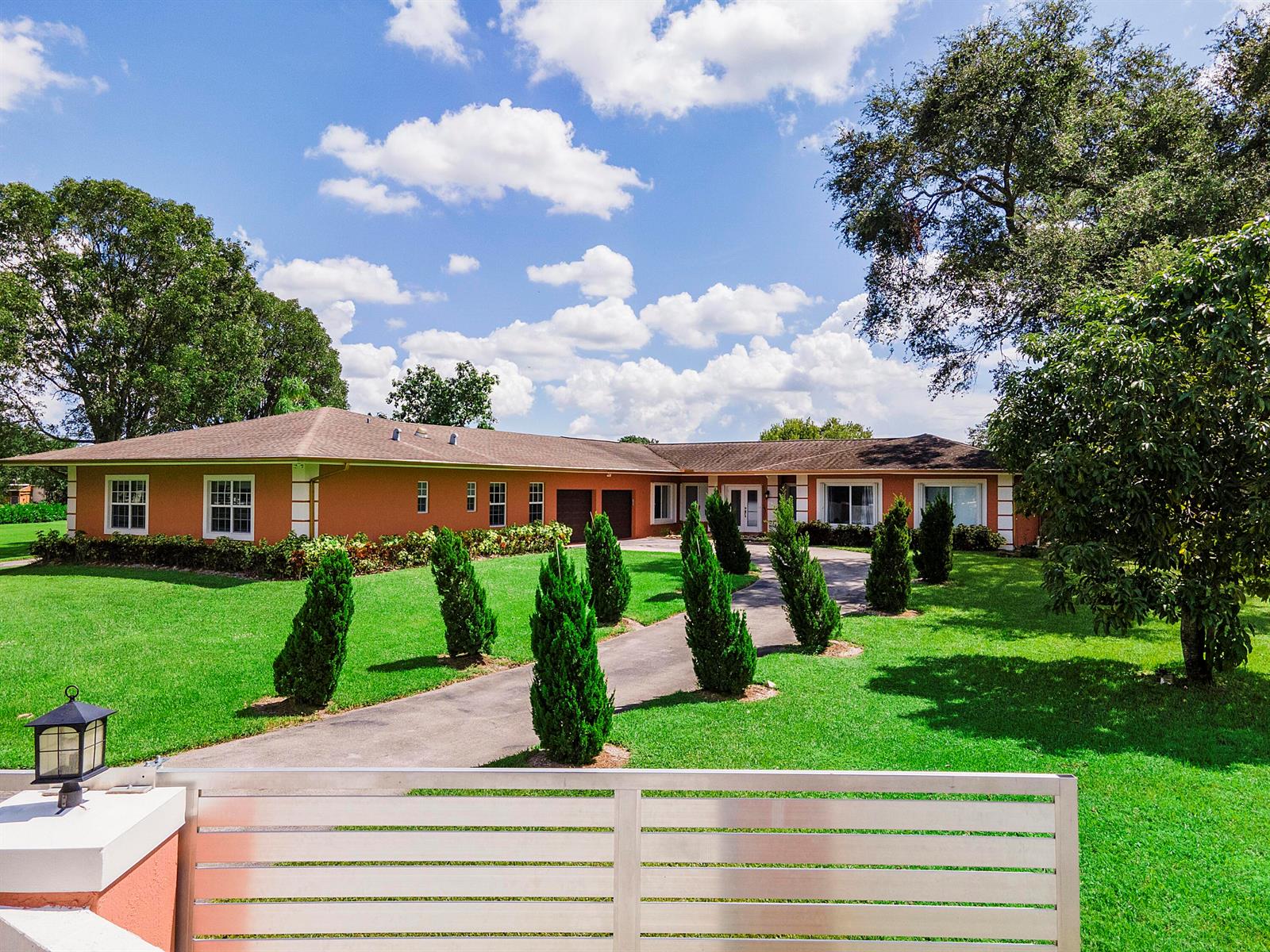 A single-story orange house with a paved driveway lined by small evergreen trees — 7600 NW 82nd Terrace, Parkland FL 33067, PARKLAND, FL