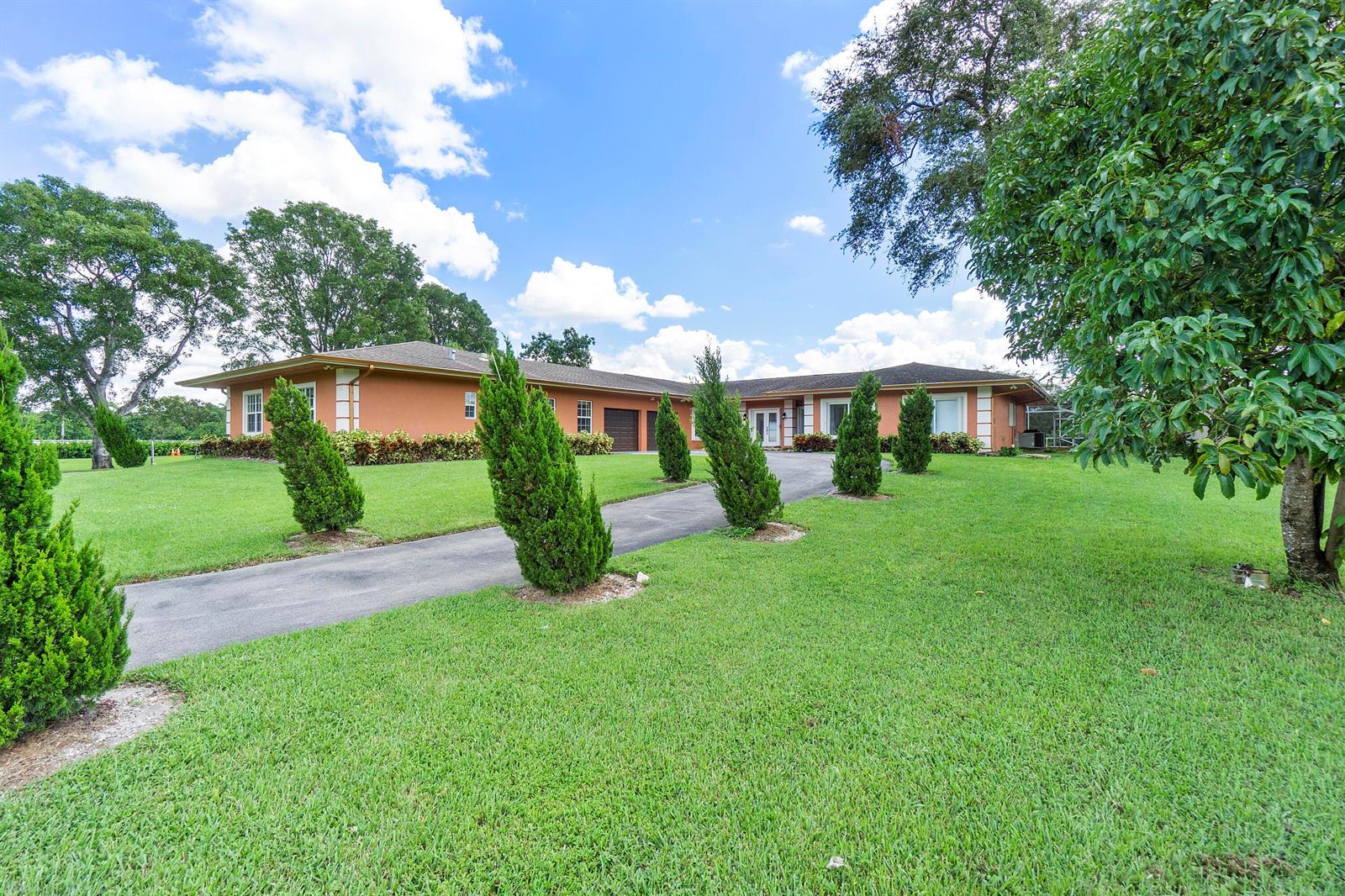 A long, single-story orange house with a driveway lined by small evergreen trees — 7600 NW 82nd Terrace, Parkland FL 33067, PARKLAND, FL