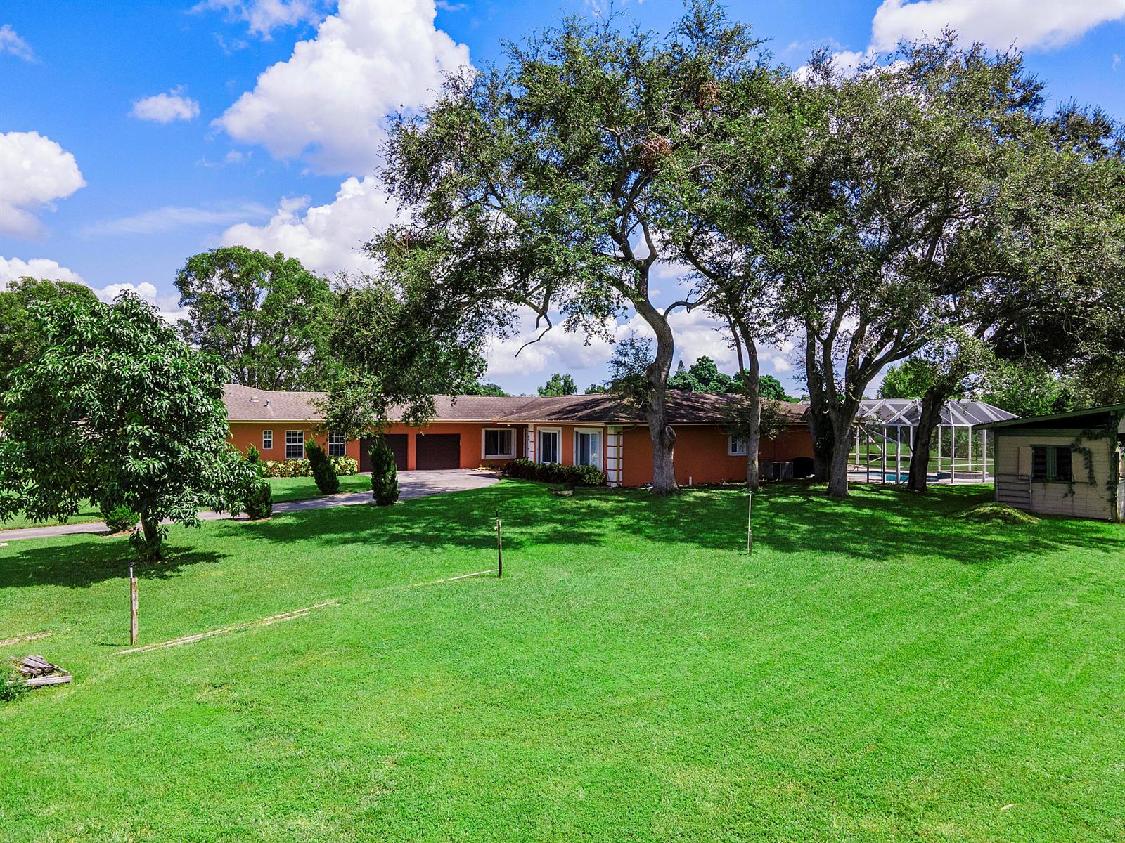 An orange single-story house with a large lawn, mature trees, and a screened pool enclosure — 7600 NW 82nd Terrace, Parkland FL 33067, PARKLAND, FL