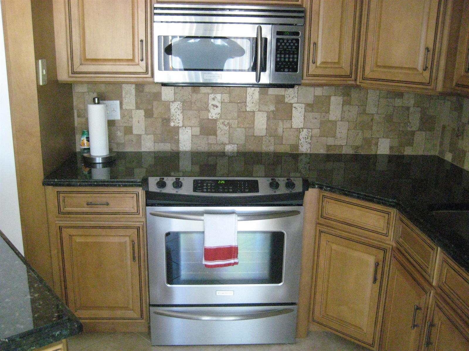 A kitchen features wood cabinets, a dark granite countertop, stainless steel appliances, and tiled backsplash — 3900 SE County Line Road # 24d, Tequesta FL 33469, TEQUESTA, FL