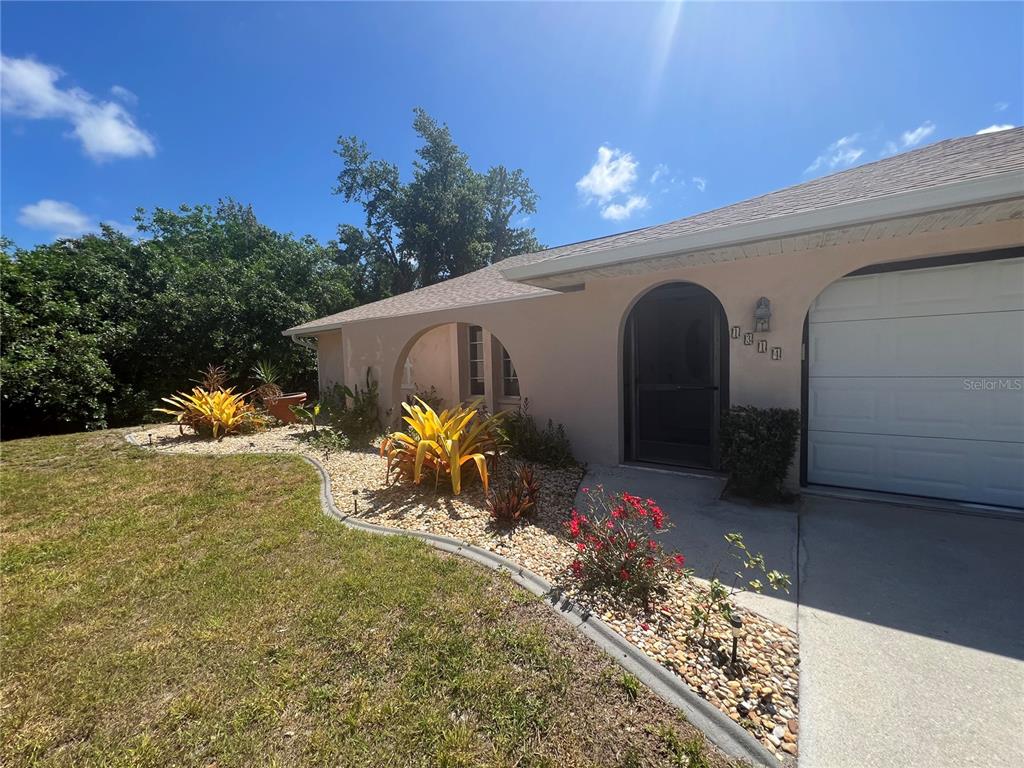 A beige house exterior features an arched entryway, a garage, and a landscaped rock garden — 1314 BEACON DRIVE, PORT CHARLOTTE, FL