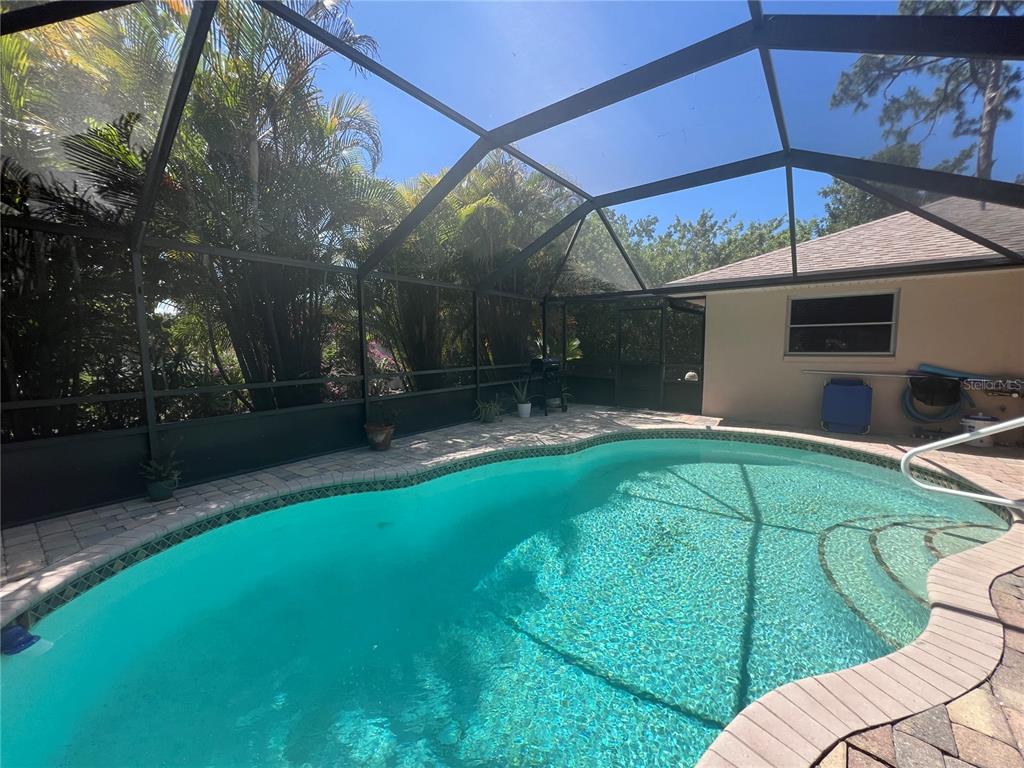 A screened-in swimming pool with a paver deck sits beside a house with a tiled roof — 1314 BEACON DRIVE, PORT CHARLOTTE, FL