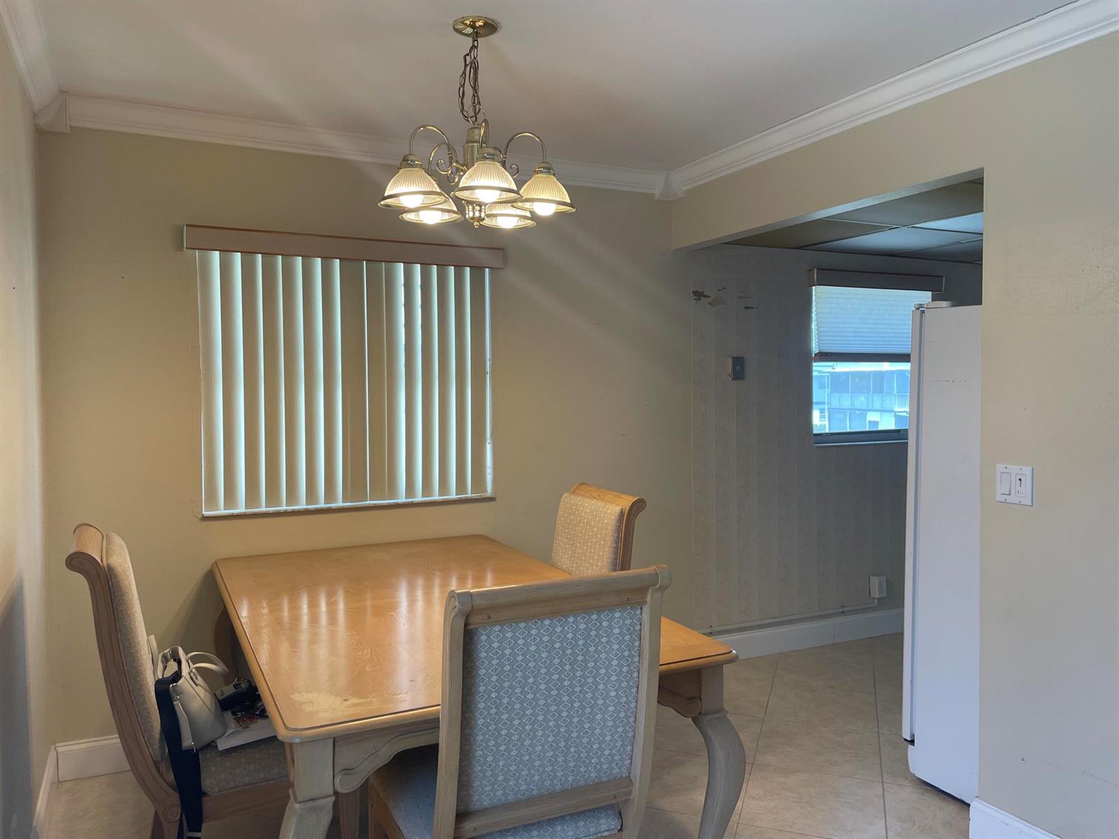 A dining area features a wooden table, upholstered chairs, a chandelier, and a window — 564 Brittany L, Delray Beach FL 33446, DELRAY BEACH, FL