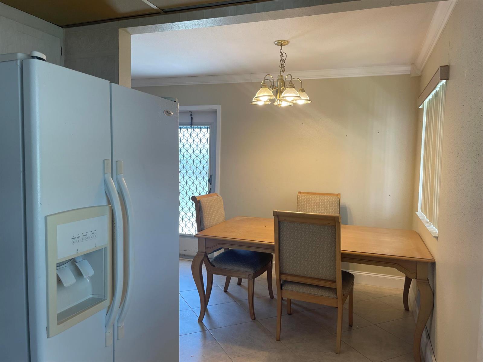A dining area features a wooden table, four upholstered chairs, a chandelier, and a white refrigerator — 564 Brittany L, Delray Beach FL 33446, DELRAY BEACH, FL