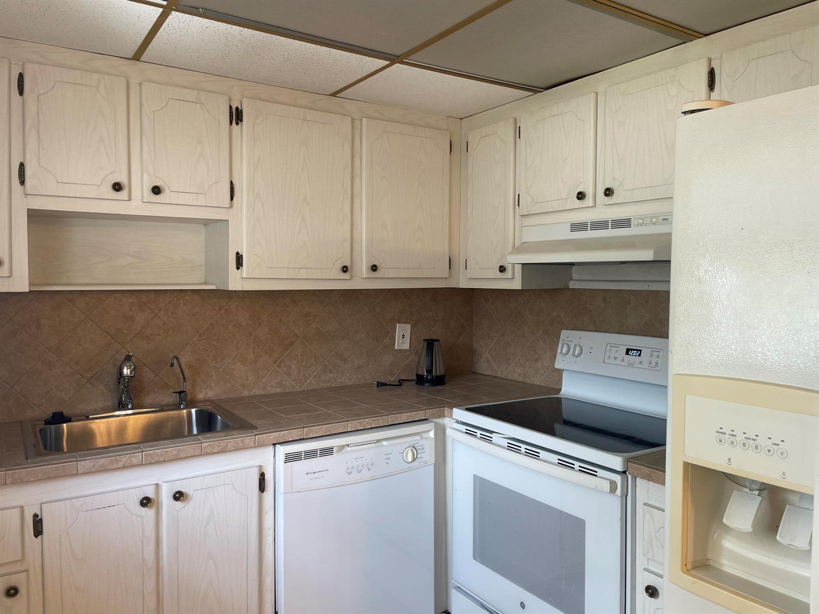 A kitchen features light wood cabinets, tile countertops, a white dishwasher, and a white stove — 564 Brittany L, Delray Beach FL 33446, DELRAY BEACH, FL