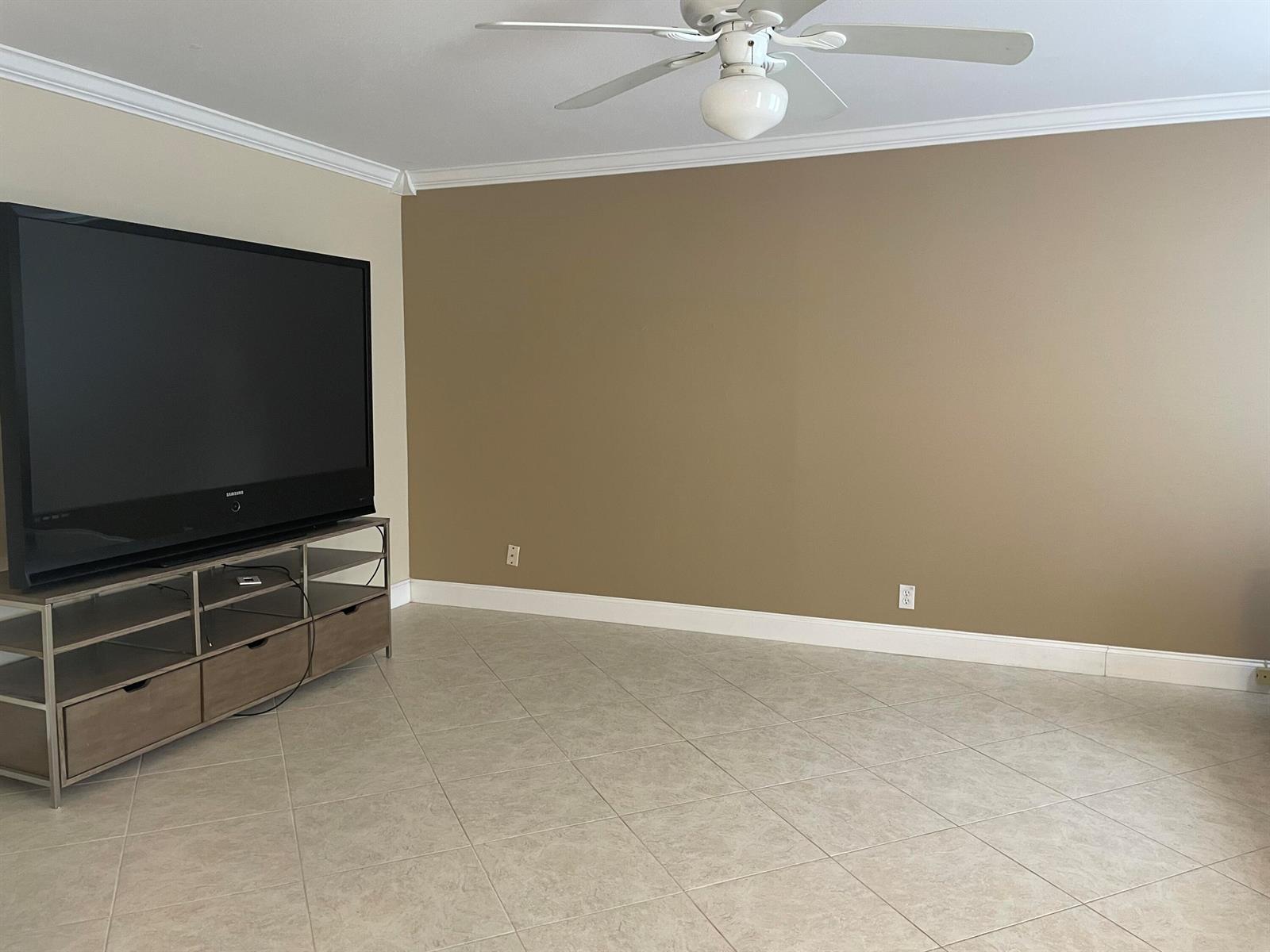 A living room features a large television on a stand against a tan wall — 564 Brittany L, Delray Beach FL 33446, DELRAY BEACH, FL