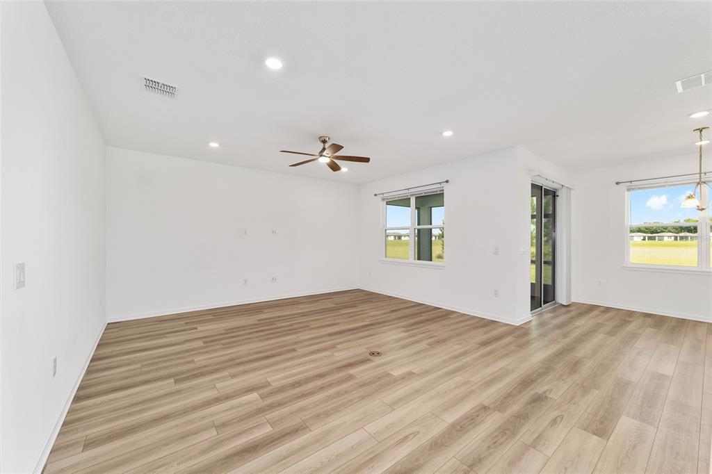 An empty living room features light wood-look flooring, white walls, a ceiling fan, and windows — 8479 SW 52ND LANE ROAD, OCALA, FL