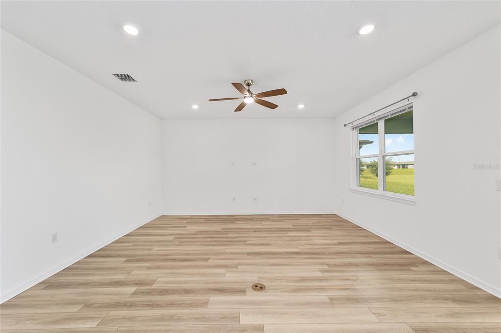 An empty living room features white walls, light wood-look flooring, a ceiling fan, and windows — 8479 SW 52ND LANE ROAD, OCALA, FL