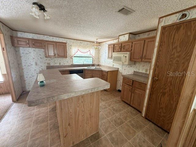 A kitchen features wood cabinets, a peninsula countertop, and patterned wallpaper — 18627 NW 24TH AVENUE, CITRA, FL