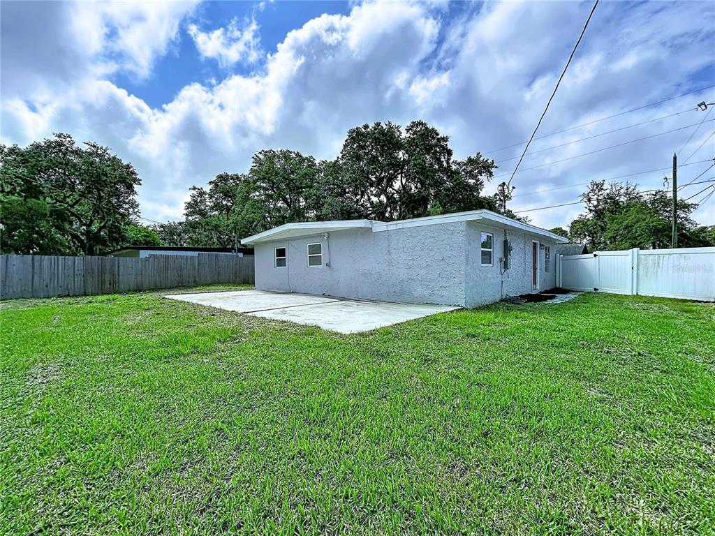 The exterior of a gray, single-story house features a concrete patio and a fenced backyard — 5005 AVERY ROAD, NEW PORT RICHEY, FL
