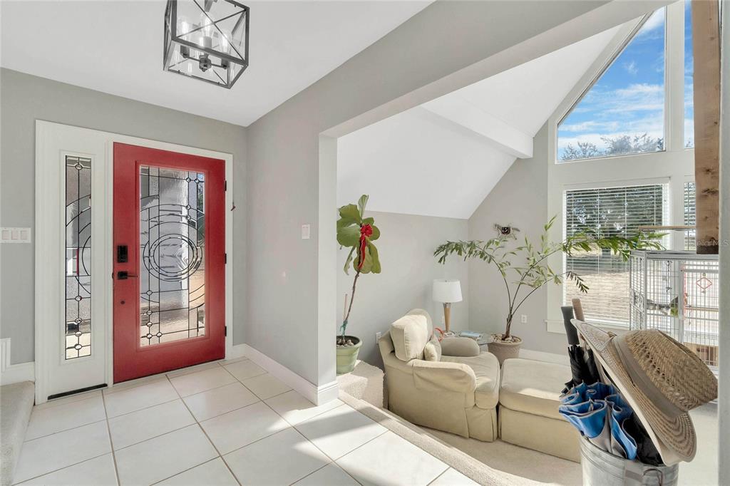 An entryway with white tile floors, a red front door, and an adjacent sunlit seating area — 16131 JOHNS LAKE ROAD, CLERMONT, FL
