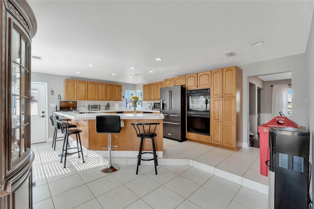 A kitchen with light wood cabinets, a tiled island with bar stools, and stainless steel appliances — 16131 JOHNS LAKE ROAD, CLERMONT, FL