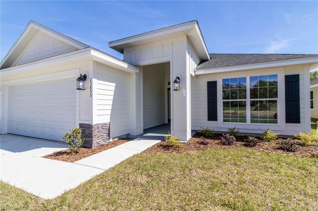A white single-story house with a garage, stone accents, and dark shutters under a blue sky — 16881 NW 176TH WAY, ALACHUA, FL