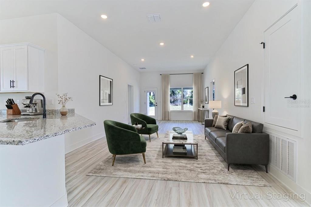 A virtually staged living room with a grey sofa, two green chairs, and light flooring — 16881 NW 176TH WAY, ALACHUA, FL