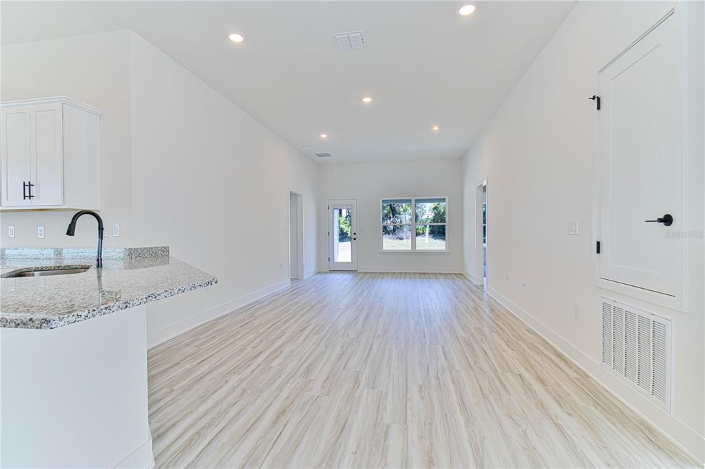 An open-concept living area features light wood-look flooring, white walls, and a granite-topped kitchen island — 16881 NW 176TH WAY, ALACHUA, FL
