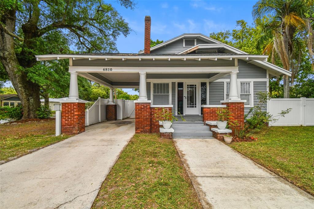 A gray bungalow with a brick-based front porch, a carport, and a concrete driveway — 6810 N NAVIN AVENUE, TAMPA, FL