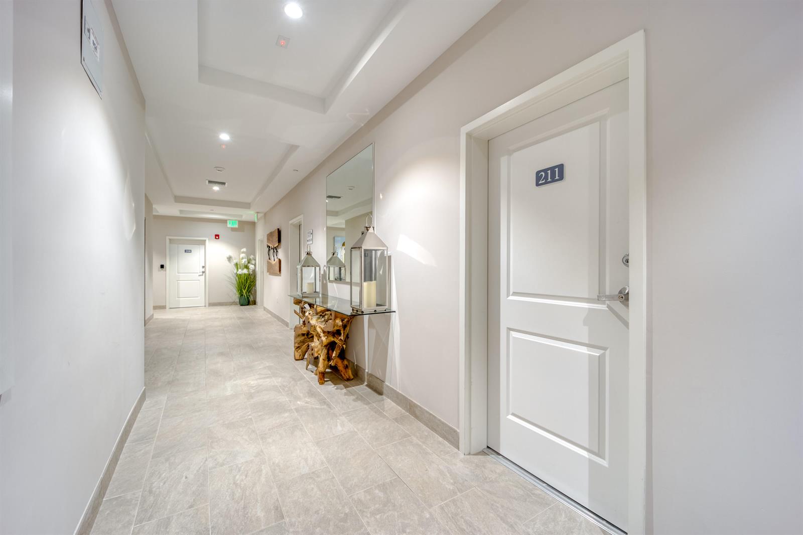 A hallway with light tile flooring, a decorative wood console table, and room 211 — 41 SW Seminole Street # 211, Stuart FL 34994, STUART, FL