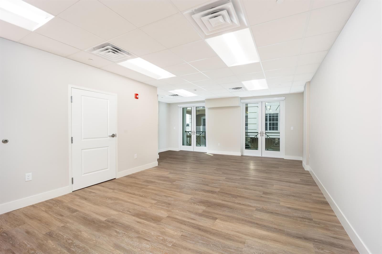 An empty office space features light wood-look flooring, white walls, and two sets of glass doors — 41 SW Seminole Street # 211, Stuart FL 34994, STUART, FL