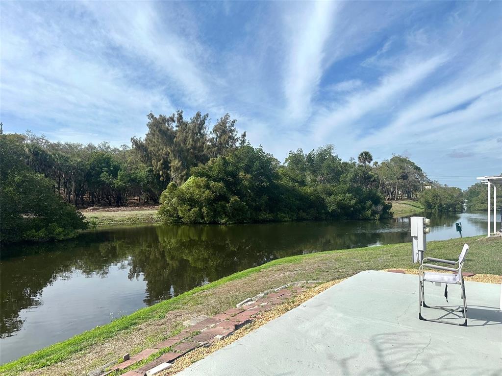 A patio overlooks a pond surrounded by trees under a blue sky — 9790 66TH STREET N UNIT 144, PINELLAS PARK, FL