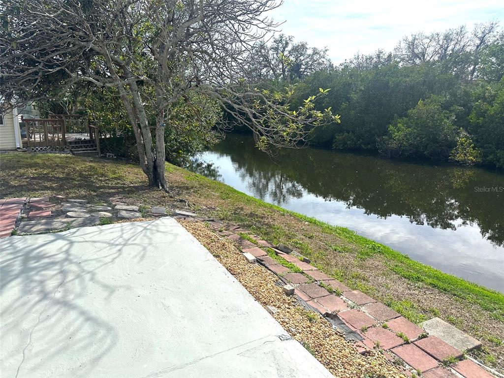 A concrete patio overlooks a canal bordered by trees and a brick walkway — 9790 66TH STREET N UNIT 144, PINELLAS PARK, FL