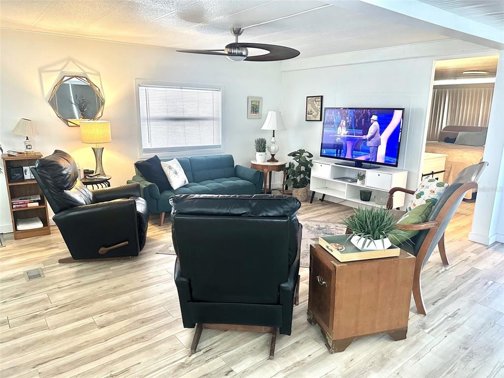 A living room features a teal sofa, two black recliners, and a television on a stand — 9790 66TH STREET N UNIT 144, PINELLAS PARK, FL